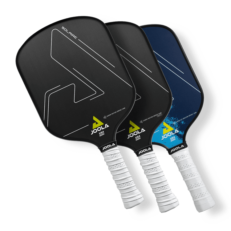 Three Joola pickleball paddles are displayed, overlapping in a fan arrangement. Each paddle has a white grip handle and a distinct design on the face, featuring minimalistic lines and logo accents in colors like black and blue.